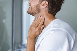 Fishman Allergy, Asthma, ENT, Thyroid self-exam checkup. Young man touching his neck at home